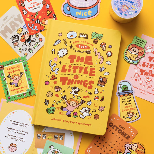 A flat-lay display of cute, cartoon-themed stationery items on a solid yellow background. The main product is a yellow hardcover notebook titled 'The Little Things' with various matching stickers, cards, and a washi tape roll arranged around it.